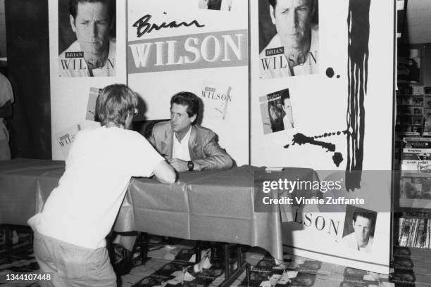 American singer, songwriter, and musician Brian Wilson signing copies of his eponymous debut solo album at an unspecified record store in Los...