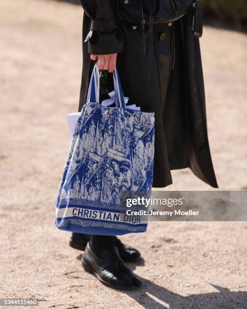 Fashion Week Guest wearing a black leather coat and a blue dior bag outside Dior on September 28, 2021 in Paris, France.