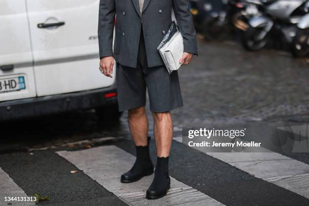 Fashion week guest wearing grey suit with short trousers, white lace top, black leather ankle boots, and white Bottega Veneta leather bag on...