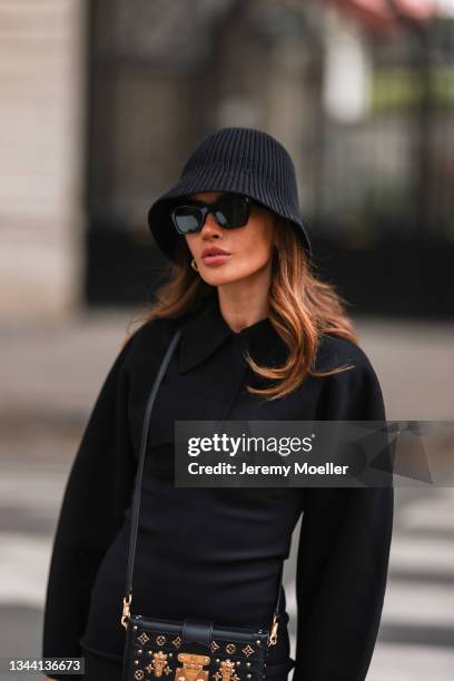 Füsun Lindner wearing black bucket hat, black midi dress, black and gold Louis Vuitton bag, and black shades on September 28, 2021 in Paris, France.