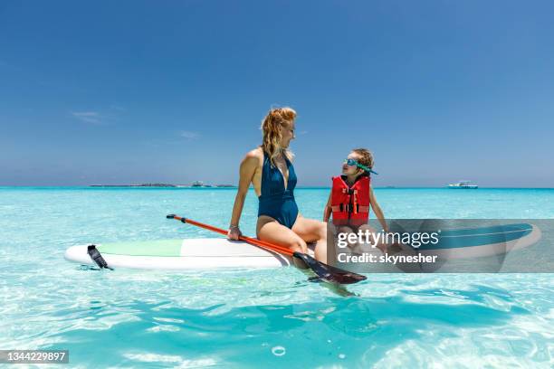 happy single mother and son talking on paddleboard at sea. - maldives boat stock pictures, royalty-free photos & images