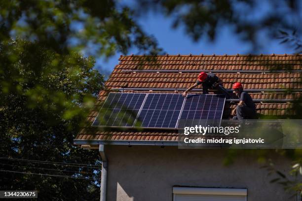 blue collar workers installing solar panels on roof of house - sunny house stock pictures, royalty-free photos & images