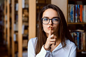 Student woman making silence gesture in a library, preventing from making loud noise in the reading room