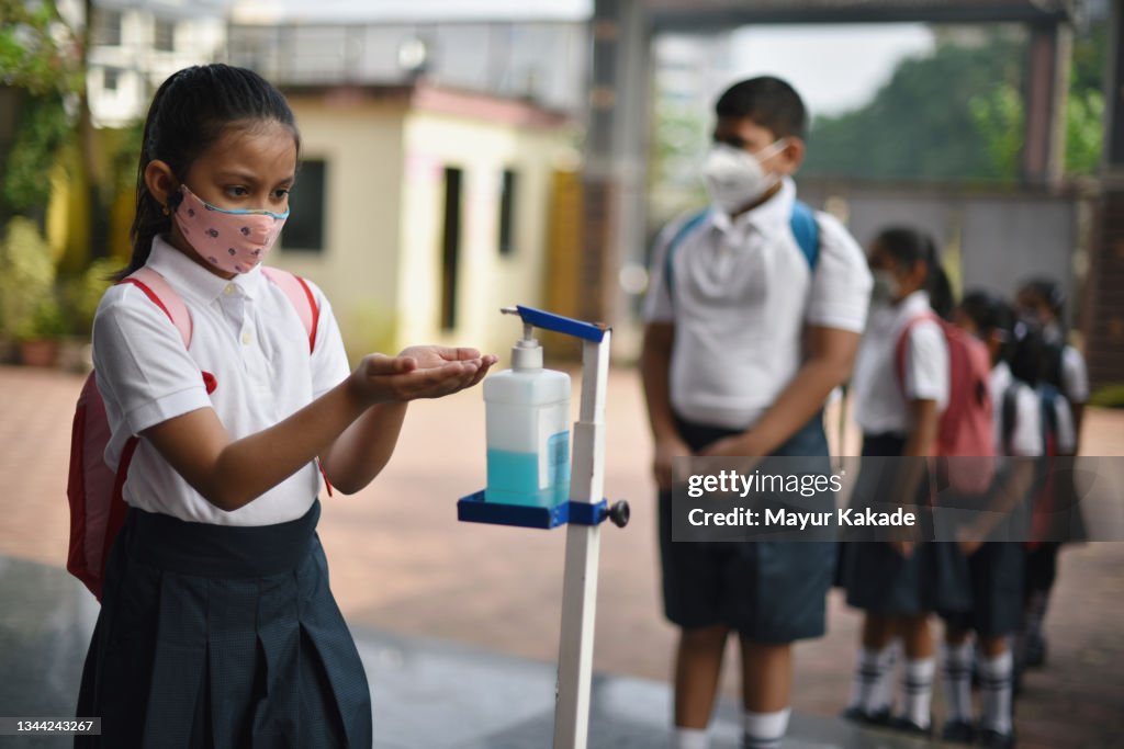 School children wearing protective masks, standing in queue and using sanitiser at the school entrance