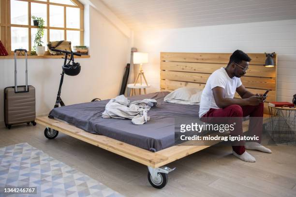 mensajes de texto de un joven mientras está sentado en la cama en casa - wood laminate flooring fotografías e imágenes de stock