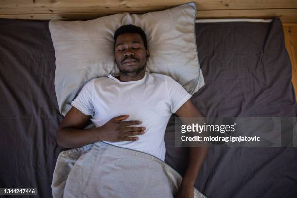 jovem dormindo na cama em casa - black man sleeping in bed - fotografias e filmes do acervo