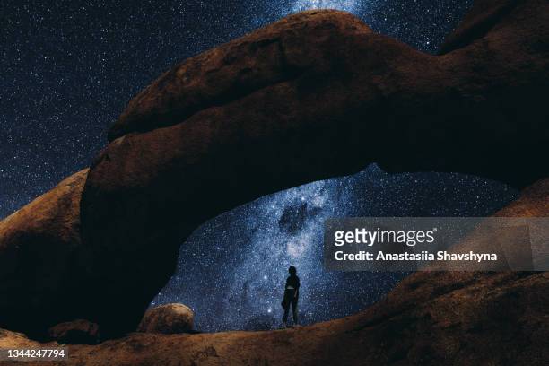 woman staying inside the natural arch looking at the million of stars in namibia - desert camping stockfoto's en -beelden