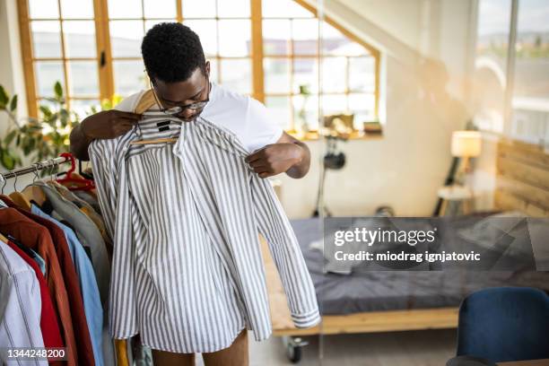 young man standing in front of clothes rack and choosing his outfit for today - clothing racks stock pictures, royalty-free photos & images