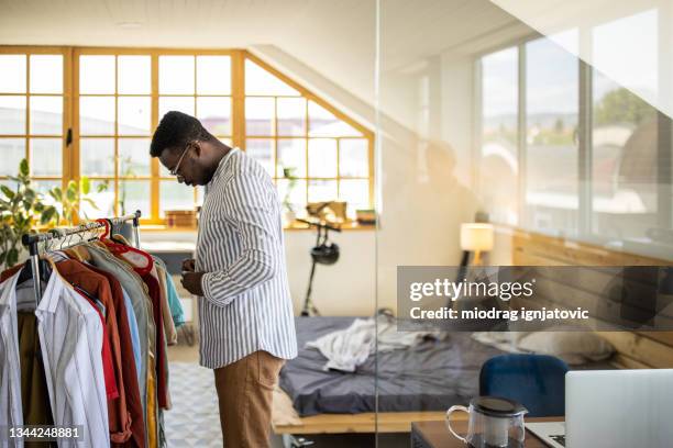 young man dressing up his shirt in bedroom - buttoning shirt stockfoto's en -beelden