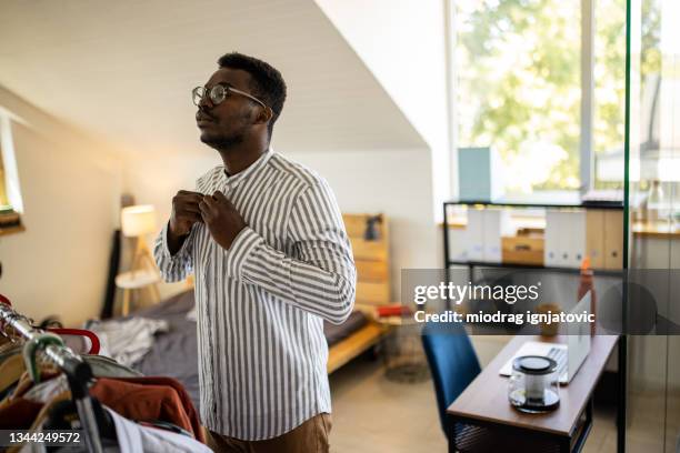 young man getting dressed and buttoning his shirt in the morning in bedroom - buttoning shirt stockfoto's en -beelden