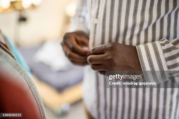 young man getting dressed and buttoning his shirt in the morning in bedroom - knäppa knappar bildbanksfoton och bilder