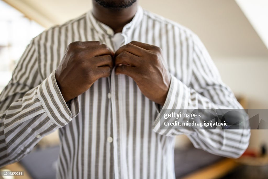 Jeune homme s’habillant et boutonnant sa chemise le matin dans la chambre
