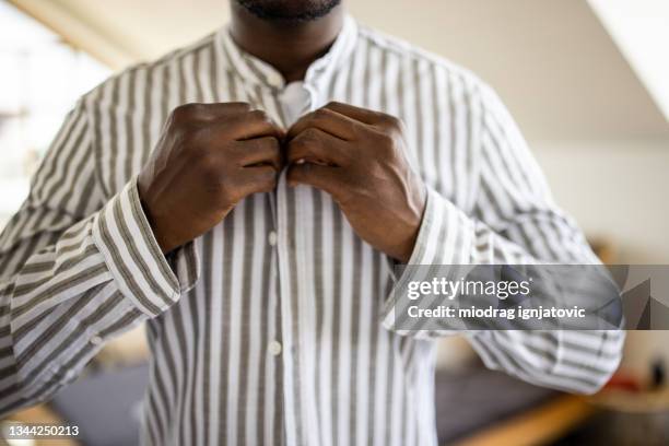 young man getting dressed and buttoning his shirt in the morning in bedroom - knäppa knappar bildbanksfoton och bilder