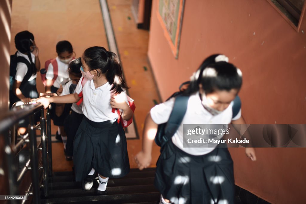 Niños en edad escolar con máscaras protectoras, caminando por la escalera del edificio escolar
