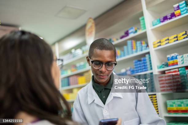 young woman showing her digital prescription on the smartphone to a young pharmacist at the phamacy - generic drug stock pictures, royalty-free photos & images