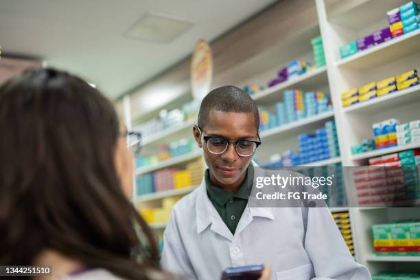 jovem mostrando sua receita digital no smartphone para um jovem farmacêutico na famacy - genérico - fotografias e filmes do acervo
