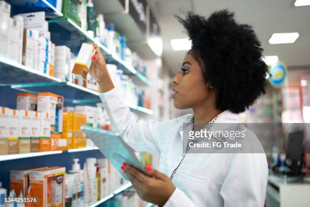 joven farmacéutico revisando los estantes con una tableta digital en la farmacia - farmacia fotografías e imágenes de stock