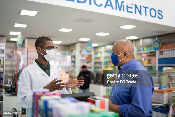 young pharmacist attending a senior man at the pharmacy - wearing a face mask - pharmacy mask stock pictures, royalty-free photos & images