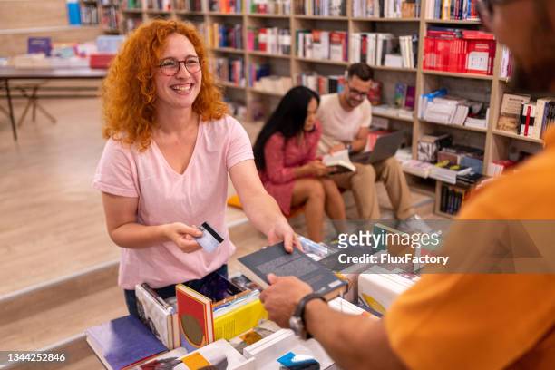 現代の書店で本の購入のためのクレジットカードで支払う興奮した赤毛��の若い女性 - bookstore ストックフォトと画像