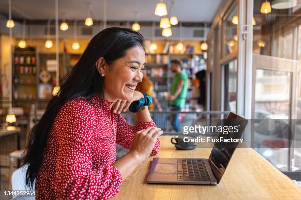 dedicated female student of asian ethnicity having online class via laptop from the modern cafeteria - diverse group of asian stockfoto's en -beelden