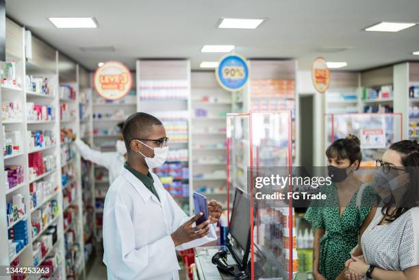 young woman showing her digital prescription on the smartphone to a young pharmacist at the pharmacy - wearing a face mask - pharmacy mask stock pictures, royalty-free photos & images