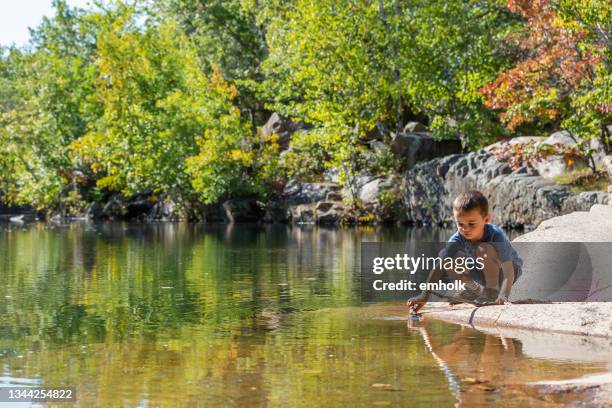 niño jugando con palo en el estanque de la cantera de granito - mia woods fotografías e imágenes de stock