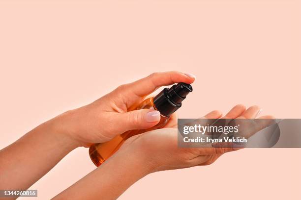 female hands holds  bottle with natural organic face serum or essential organic oil on trendy peach pink color background - cosmetic bottle stock-fotos und bilder