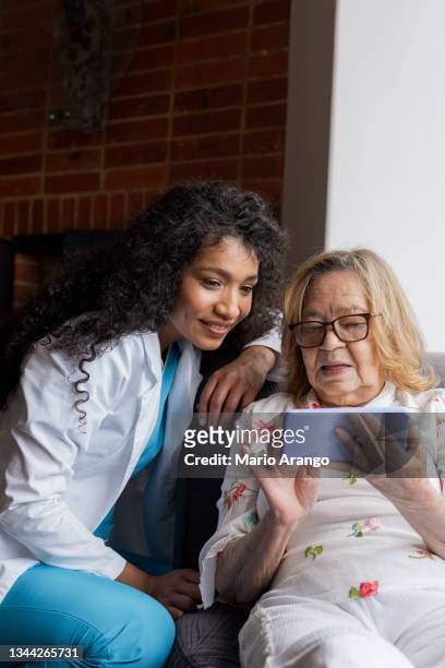 nursing assistant of an elderly man checks his patient's cell phone while showing him photos of his cell phone - doctor house call stock pictures, royalty-free photos & images