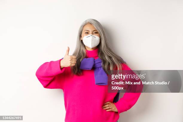 portrait of woman wearing surgical mask while gesturing against white background - casino mask stock pictures, royalty-free photos & images