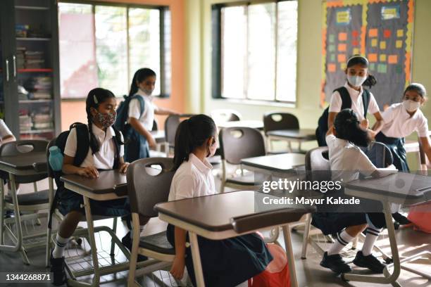 school children sitting and talking to each other in classroom with protective face masks - social distancing classroom stockfoto's en -beelden