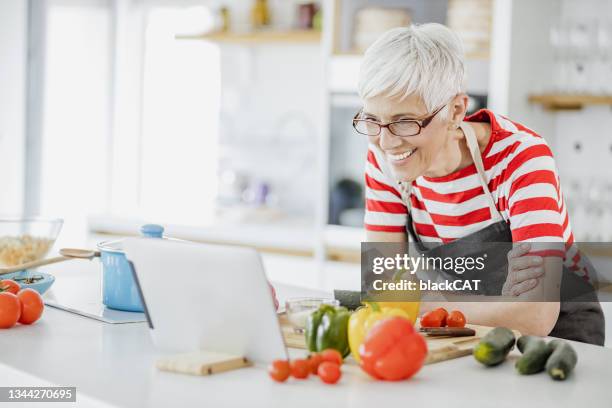 senior woman cooking at home and looking for recipes online - cooking class stock pictures, royalty-free photos & images
