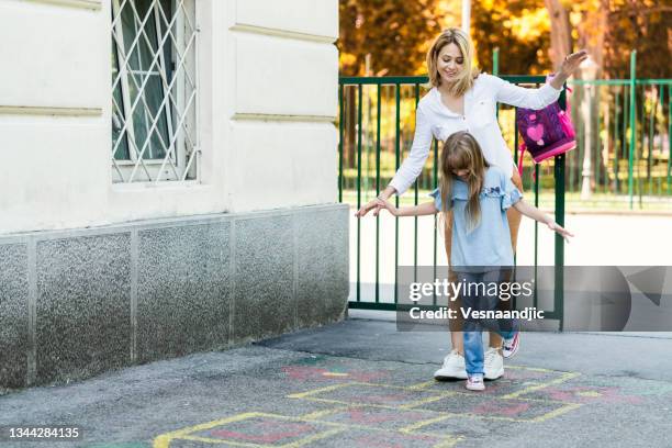 happy schoolgirl playing hopscotch with her mother on school playground outdoors - hopscotch stock pictures, royalty-free photos & images