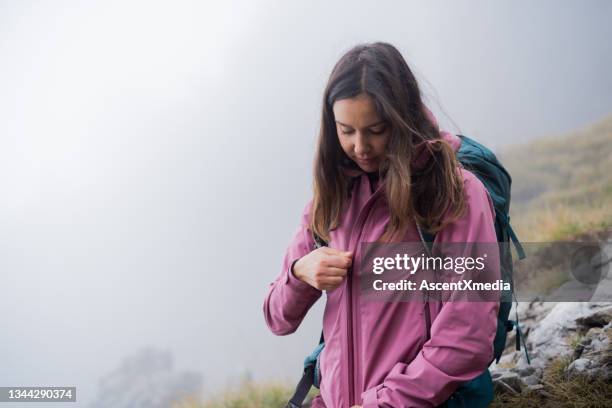 female hiker zips rain jacket up, as the fog rolls in - blixtlås bildbanksfoton och bilder