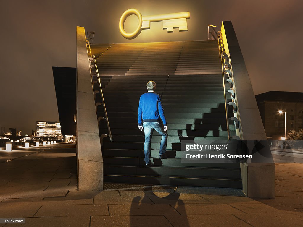 Young man on stairs looking up at giant key