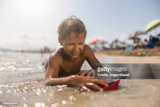 teenage boy playing with little boats on the beach - kid sailing imagens e fotografias de stock