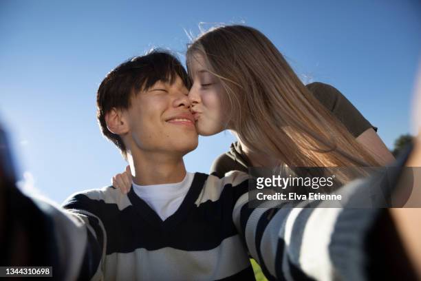 happy teenage couple taking a self portrait of themselves together outdoors against a blue cloudless sky in summertime. - young teen couple stock-fotos und bilder