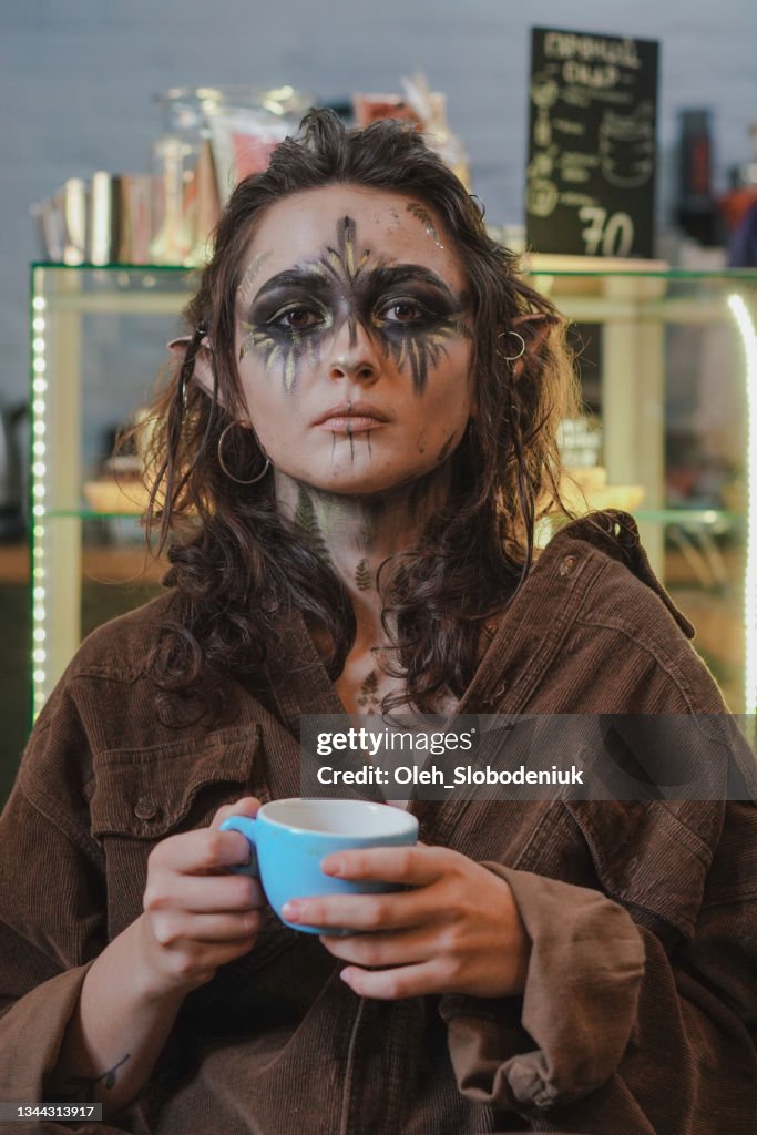 Frau im Halloween Elfenkostüm sitzend mit Tasse Kaffee im Café