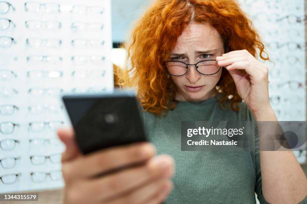 joven pelirroja con problemas de visión tratando de leer - miopía fotografías e imágenes de stock
