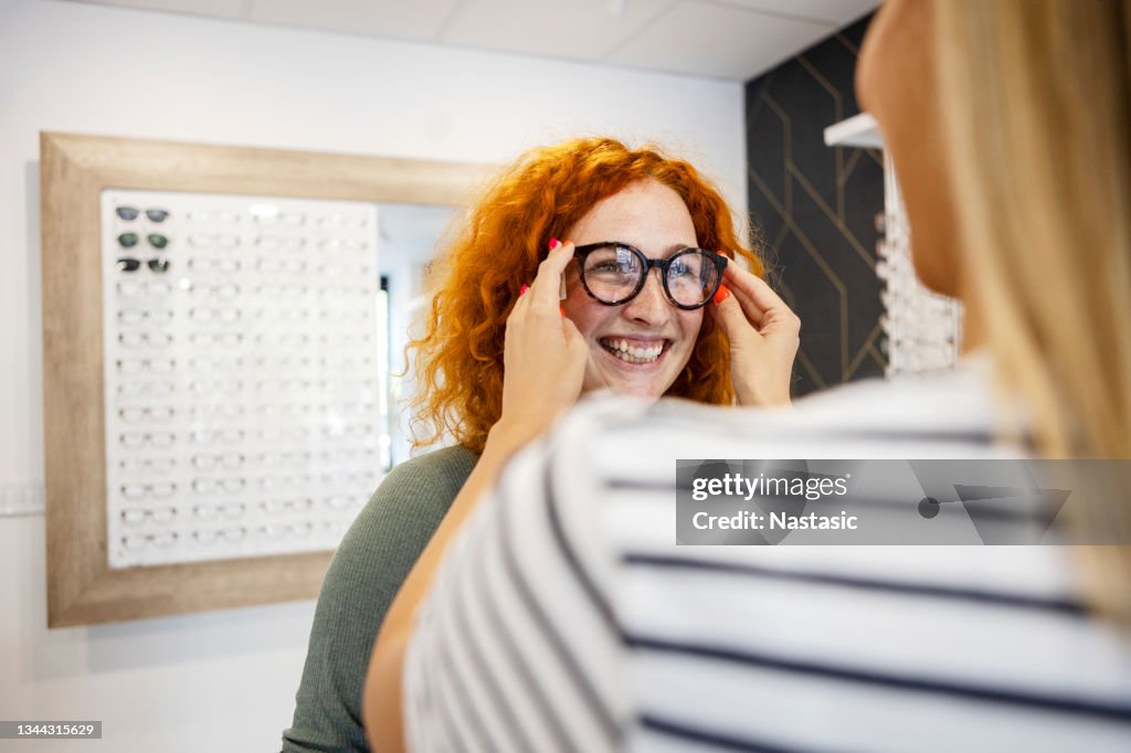 Junge Frau, die im Optikgeschäft eine Brille anlächelt, lächelt und spaßt