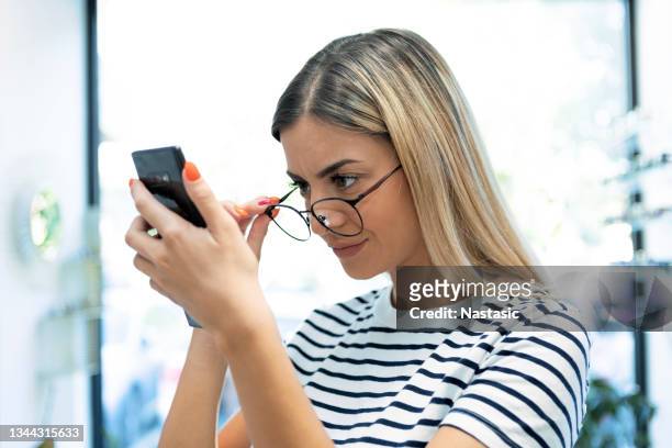 joven pelirroja con problemas de visión tratando de leer el texto del teléfono - acechar fotografías e imágenes de stock