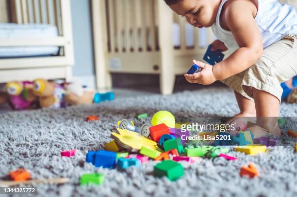 colorido lío de juguetes y niño pequeño de raza mixta - kids mess carpet fotografías e imágenes de stock