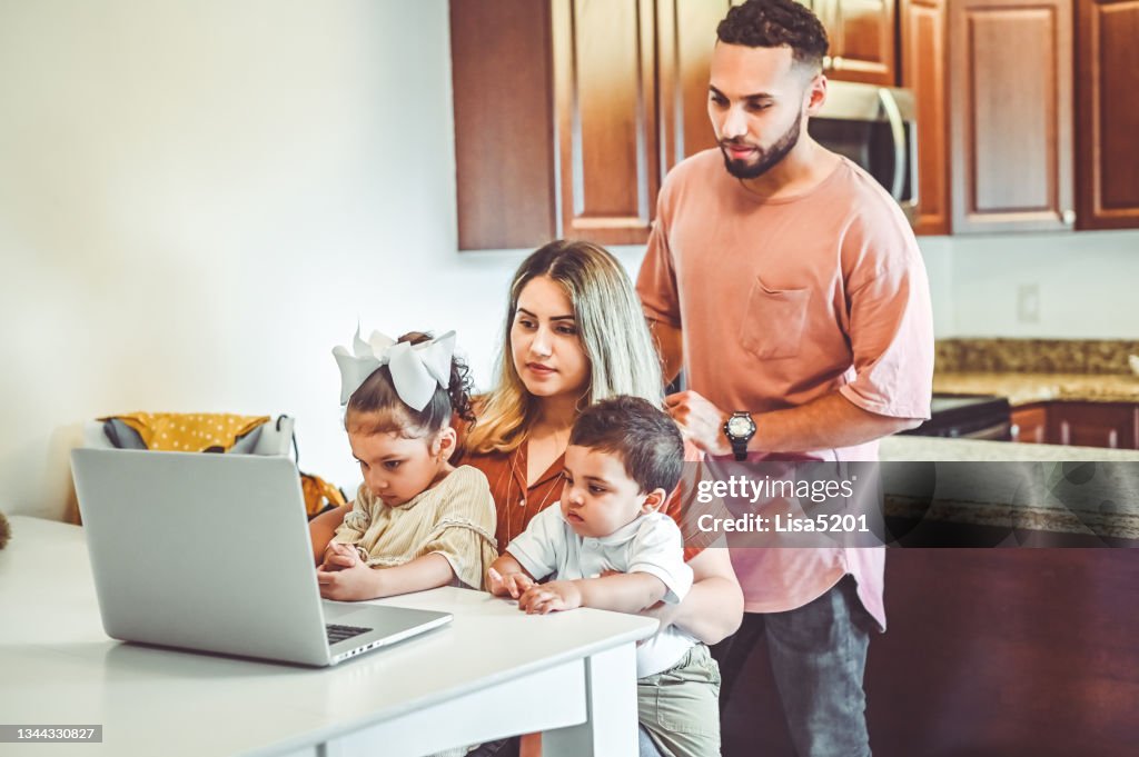 Madre y padre junto con dos niños pequeños usan una computadora portátil en un hogar familiar doméstico