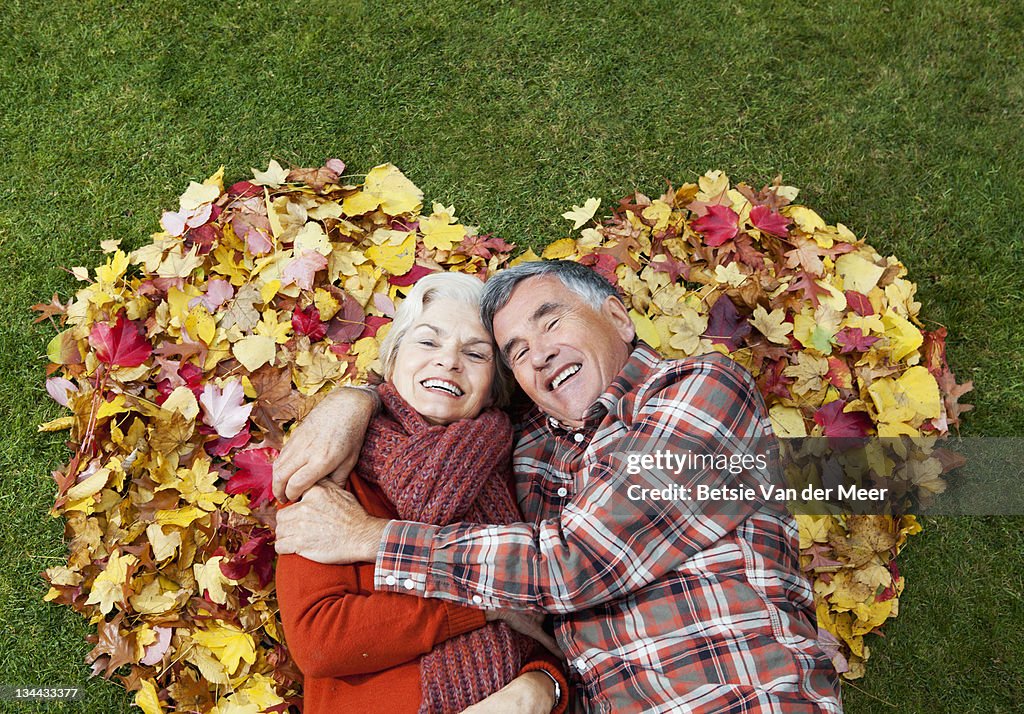 Mature couple laying in autumnal heart shape.