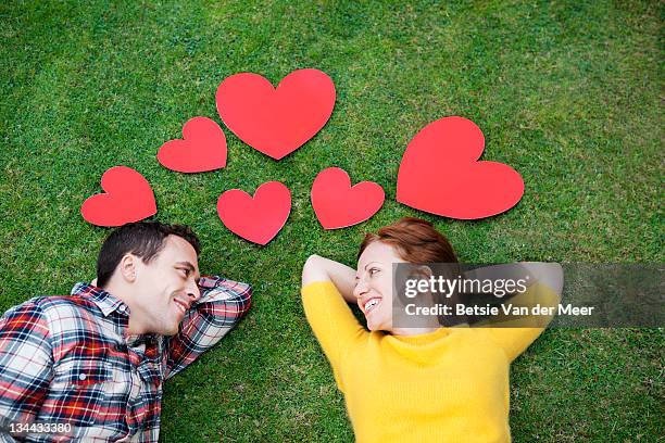 couple laying in grass,surrounded by hearts. - tomber amoureux photos et images de collection