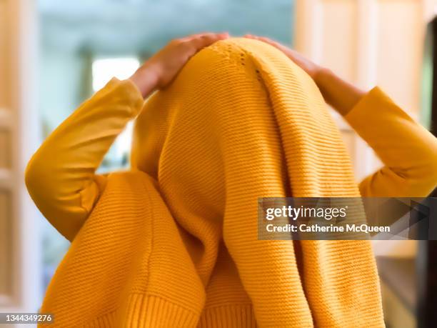 young mixed-race girl playing around with sweater covering her head instead of getting ready for school - killing time stock pictures, royalty-free photos & images