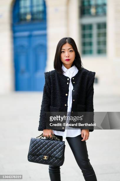 May Berthelot wears a white shirt, a black tweed jacket with epaulets, black shiny leather skinny pants, a black shiny leather Chanel handbag, a...