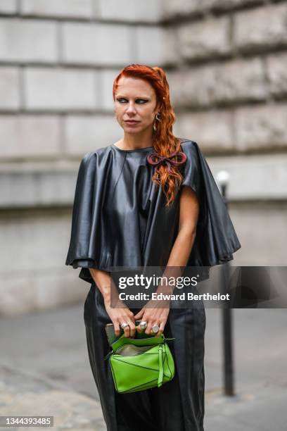 Courtney Trop wears silver earrings, a black shiny leather flowing ruffled t-shirt, matching black shiny leather high waist large pants, a green...