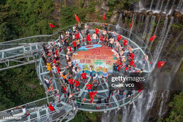 Tourists with Chinese national flags walk on a glass bridge at Gulongxia scenic spot on China's National Day on October 1, 2021 in Qingyuan,...