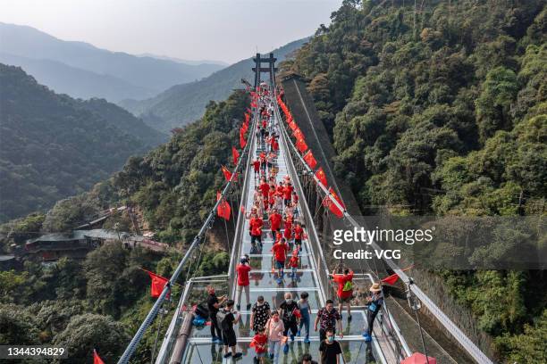 Tourists with Chinese national flagswalk on a glass bridge at Gulongxia scenic spot on China's National Day on October 1, 2021 in Qingyuan, Guangdong...