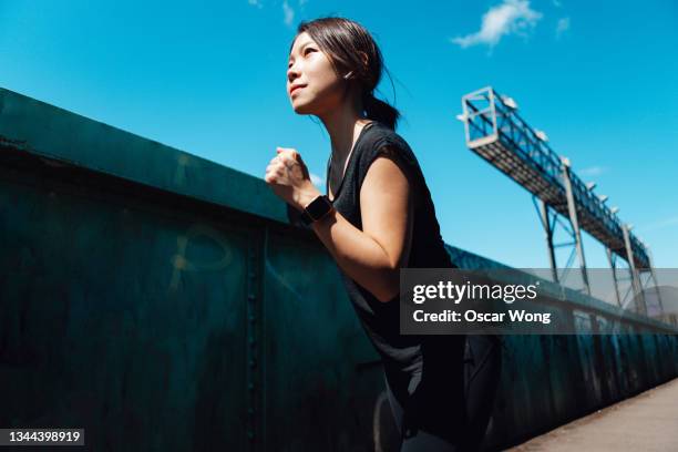 young asian woman running on footbridge against blue sky - 運動　日本人 ストックフォトと画像